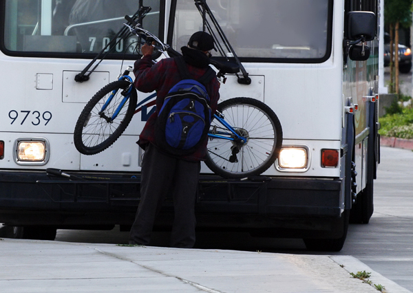 Man putting a bike on the front of a bus